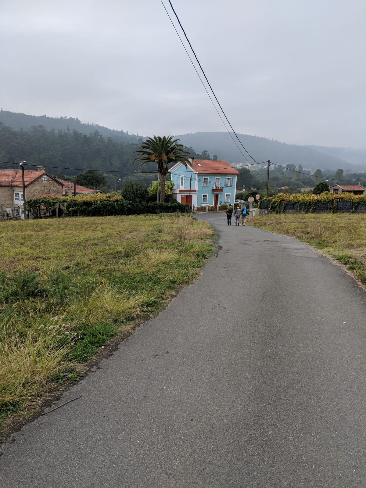 Misty road with a blue house and pilgrims ahead