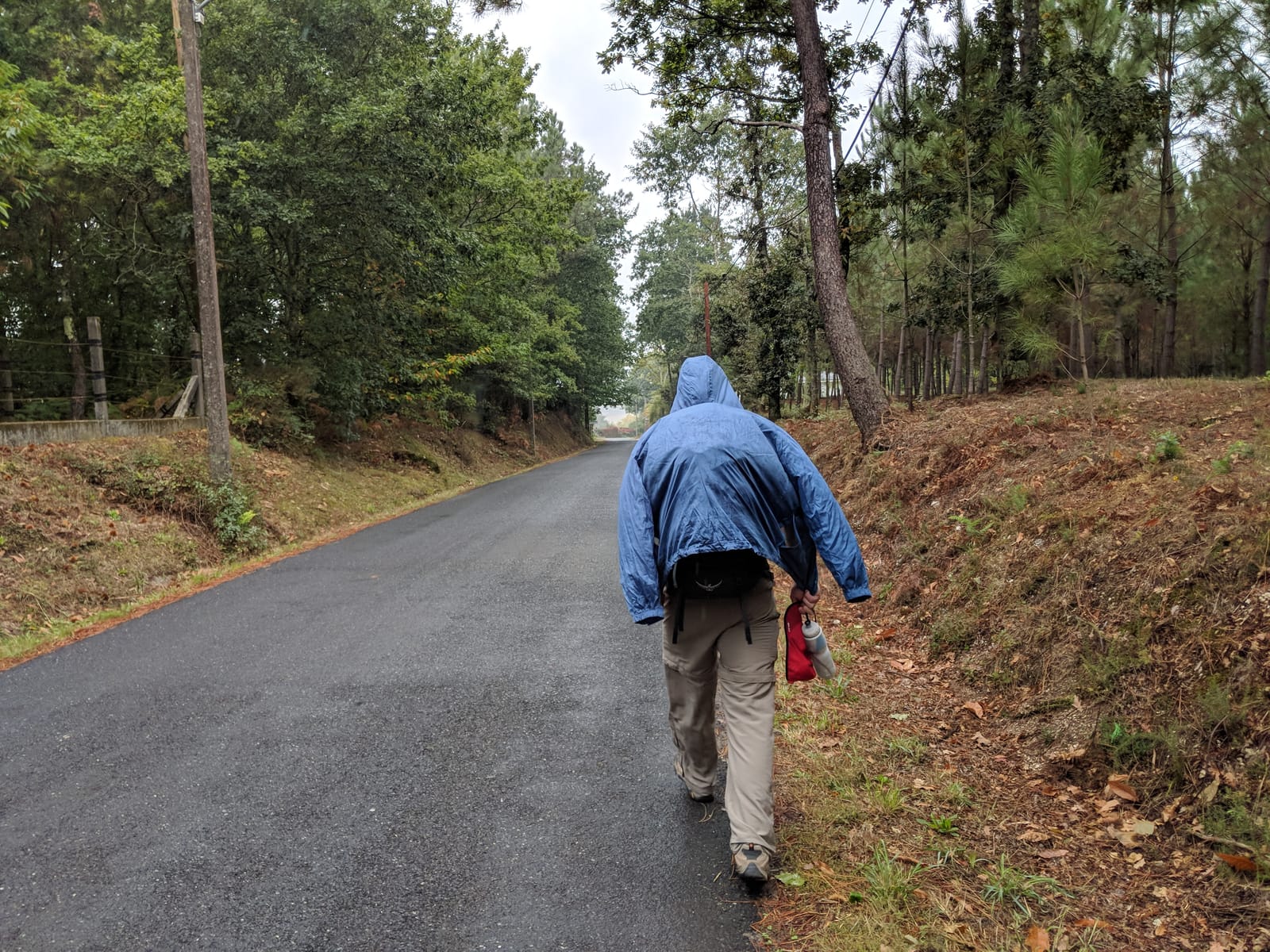 Doug walking a country road in a rain jacket under grey skies