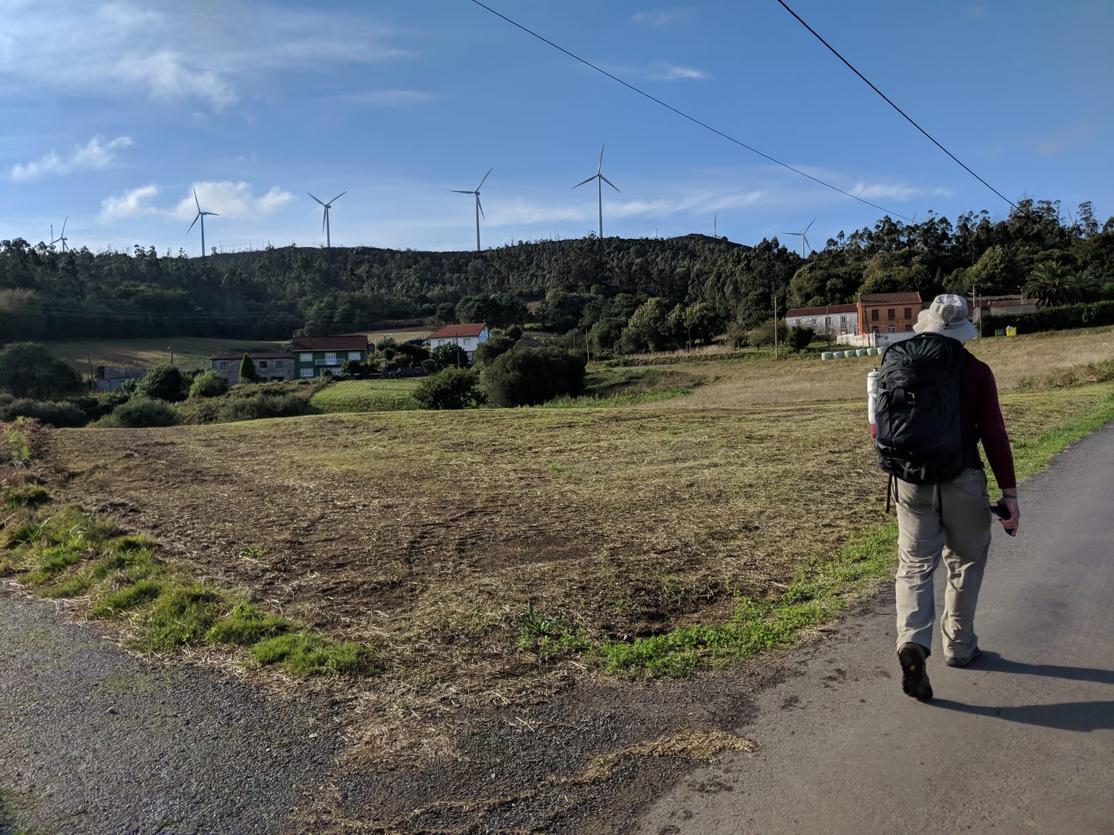 Doug walking a paved lane below a ridge lined with wind turbines