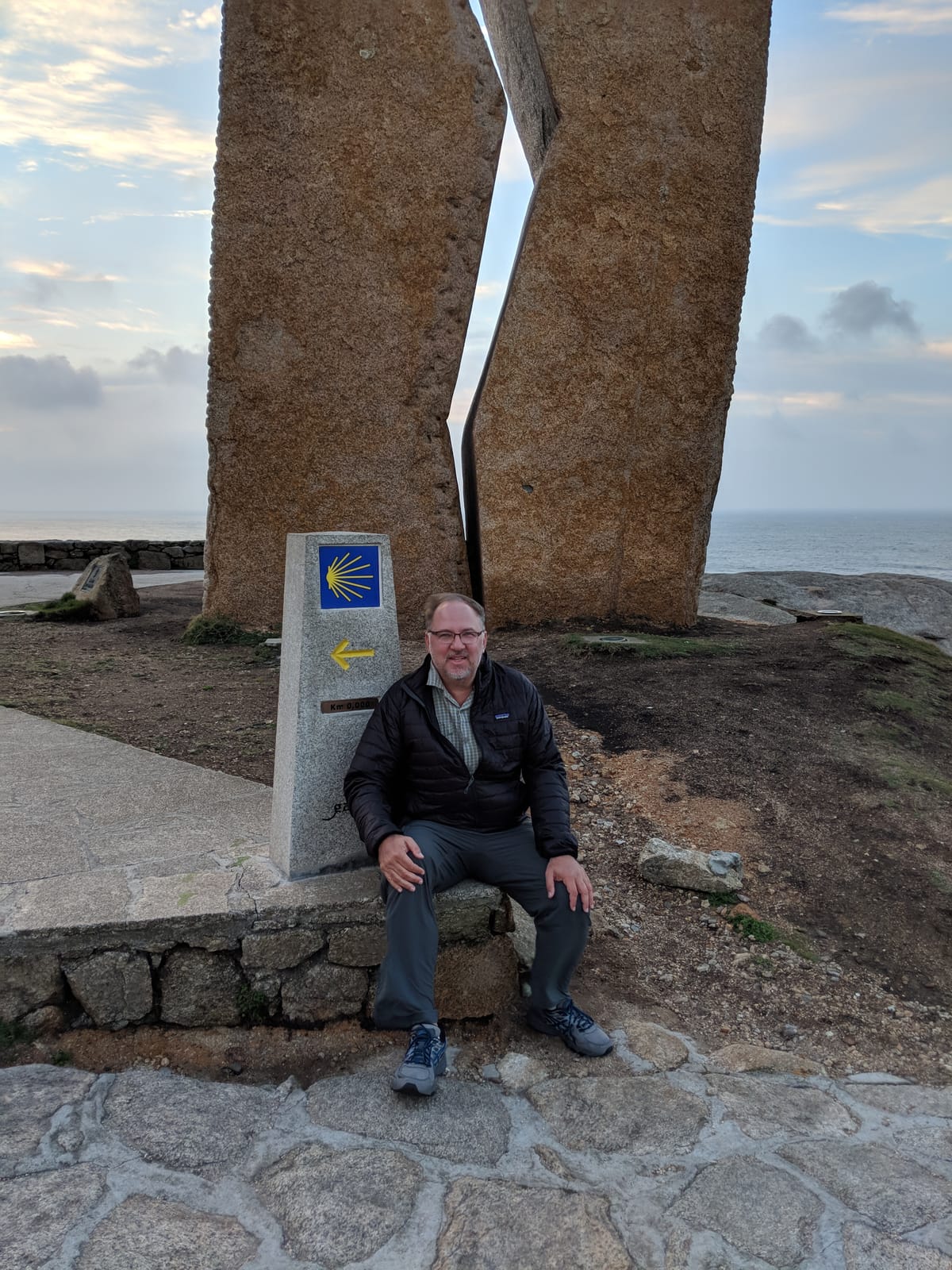 A Ferida sculpture with the Km 0,000 Camino waymarker at its base beside the sea