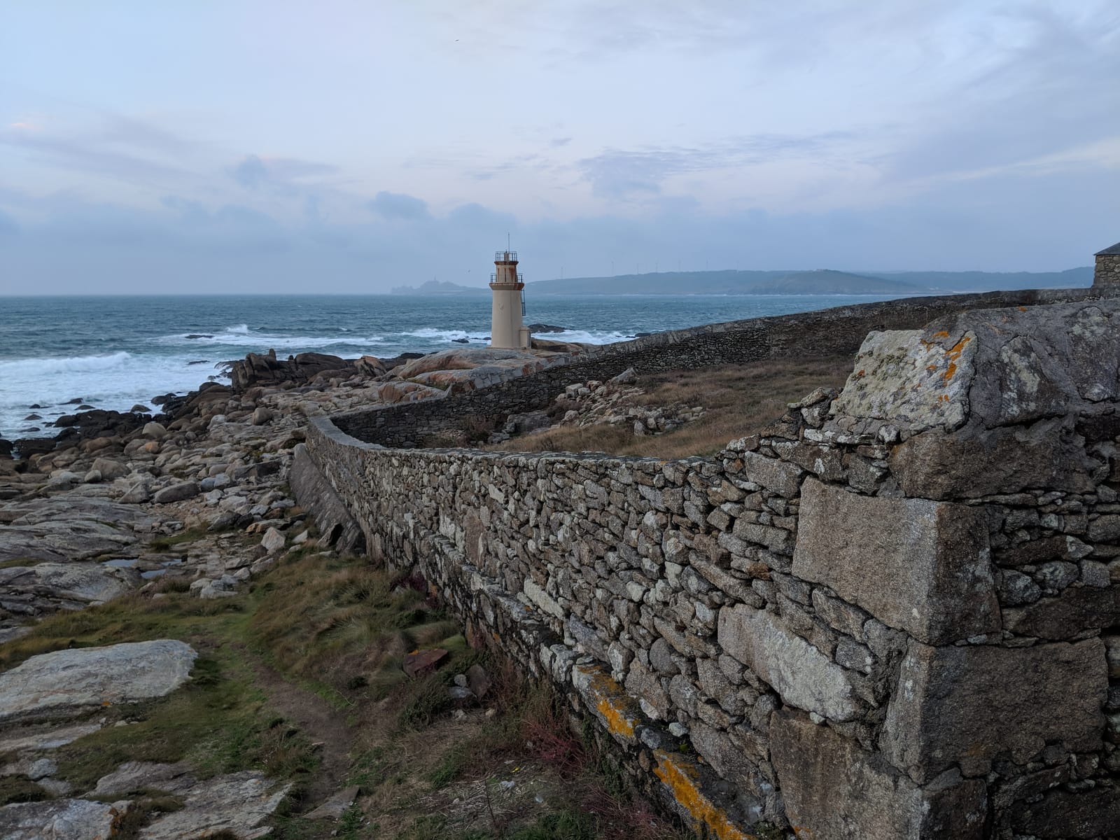 The lighthouse on the rocky point at Muxía with dry-stone walls and the Atlantic beyond