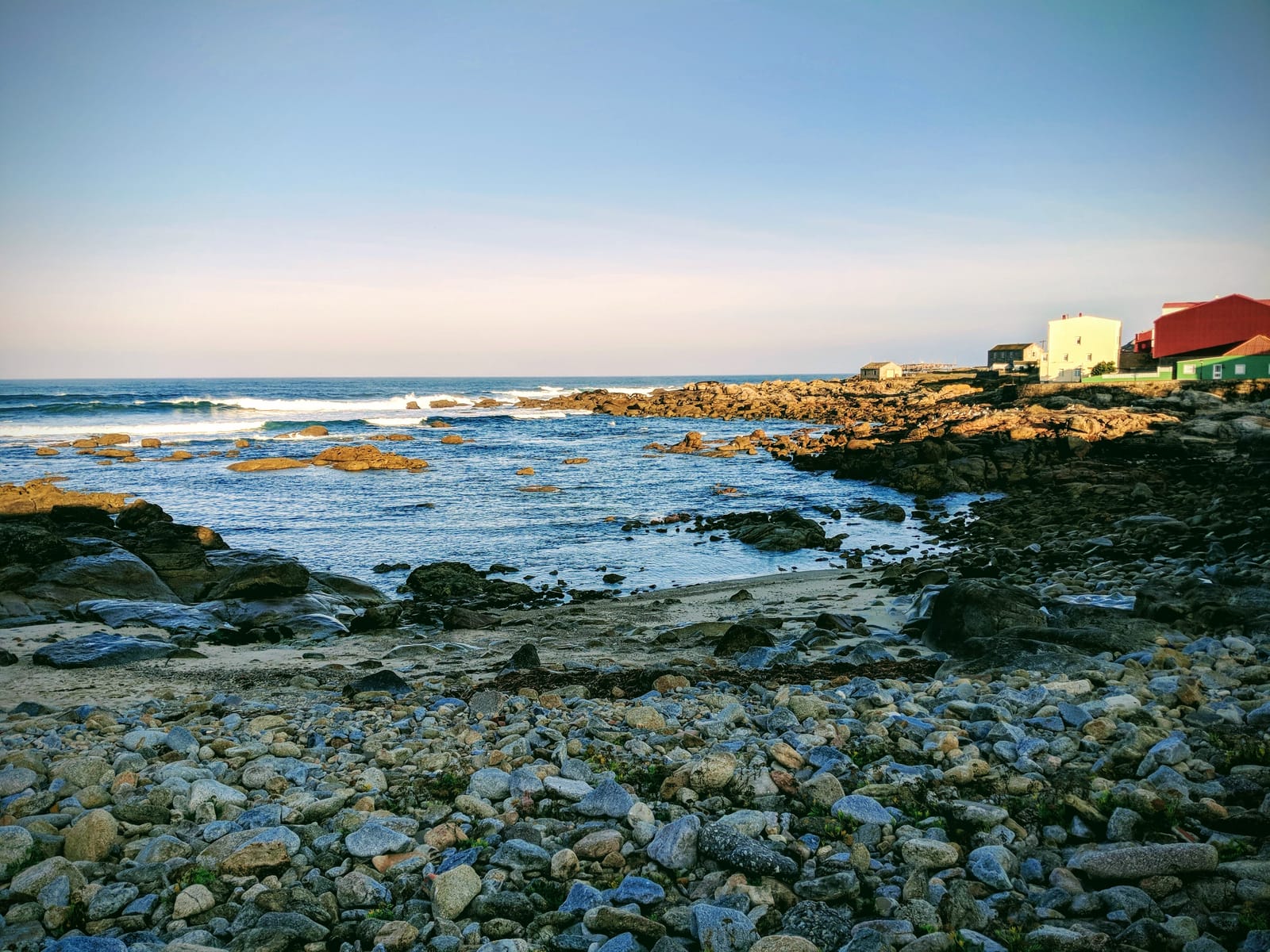 Rocky boulder beach on the edge of Muxía in the early morning, houses on the point beyond