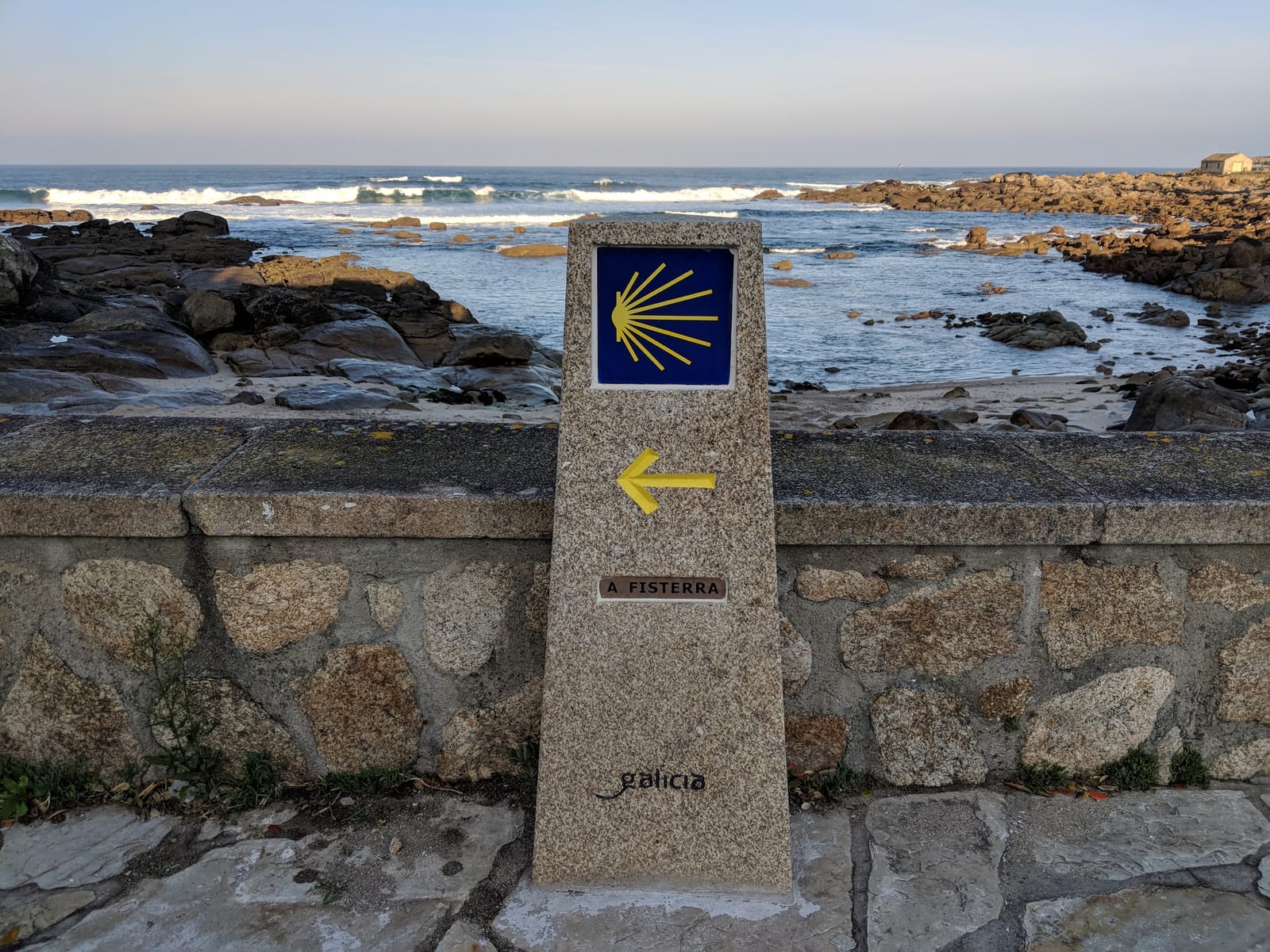 A granite Camino waymarker reading A FISTERRA with a yellow arrow beside the shore