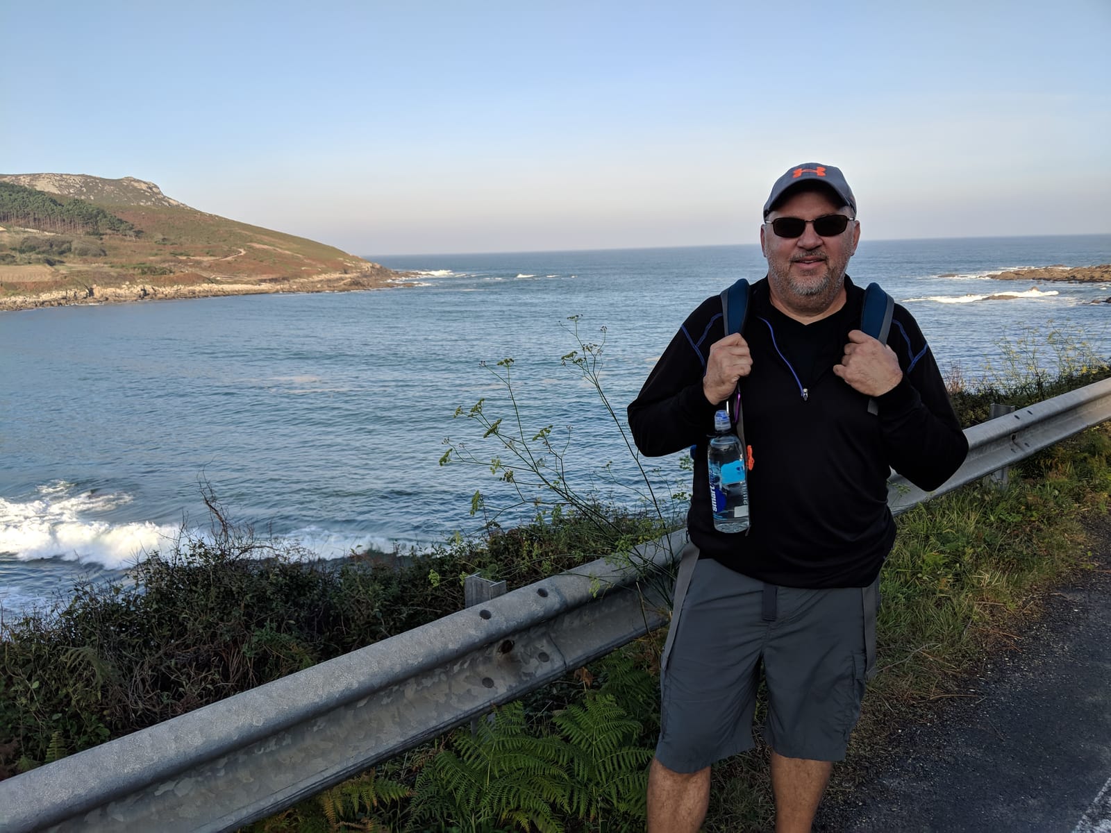 Mike posing at a guardrail with the coast and a headland behind