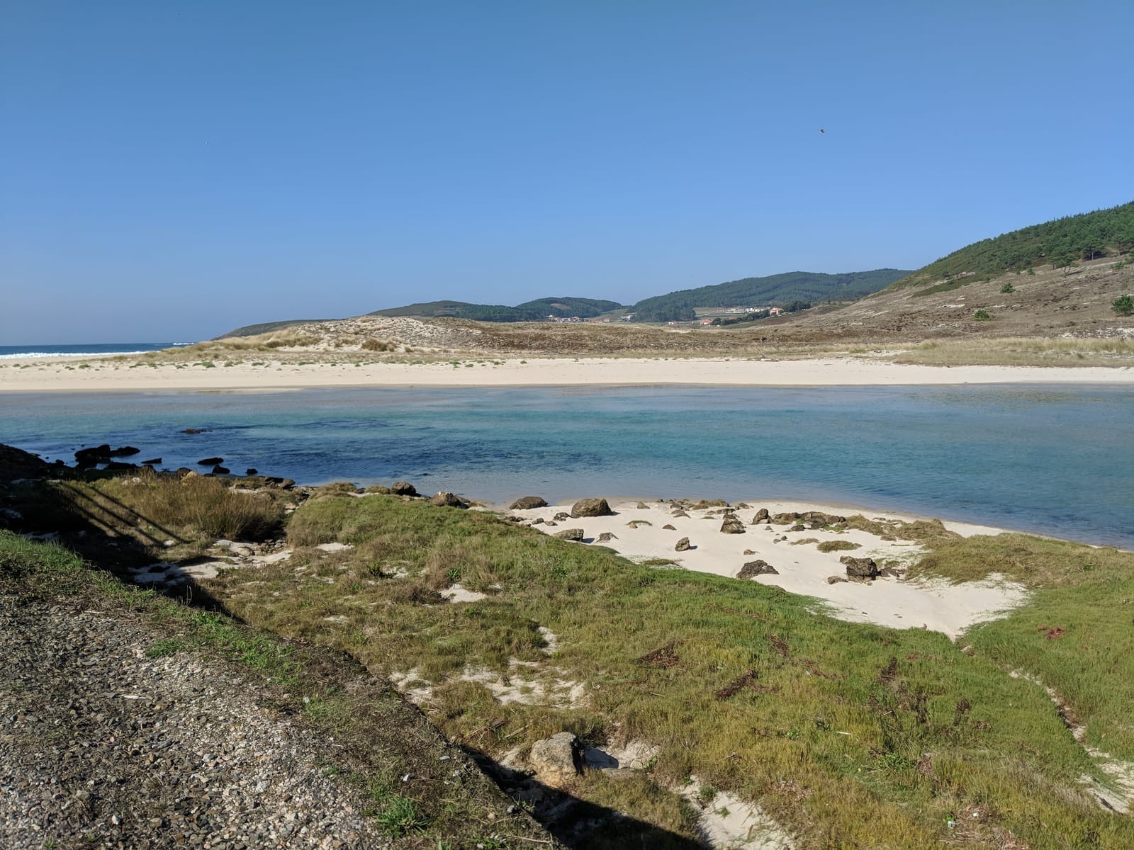 Turquoise lagoon behind sand dunes with hills beyond