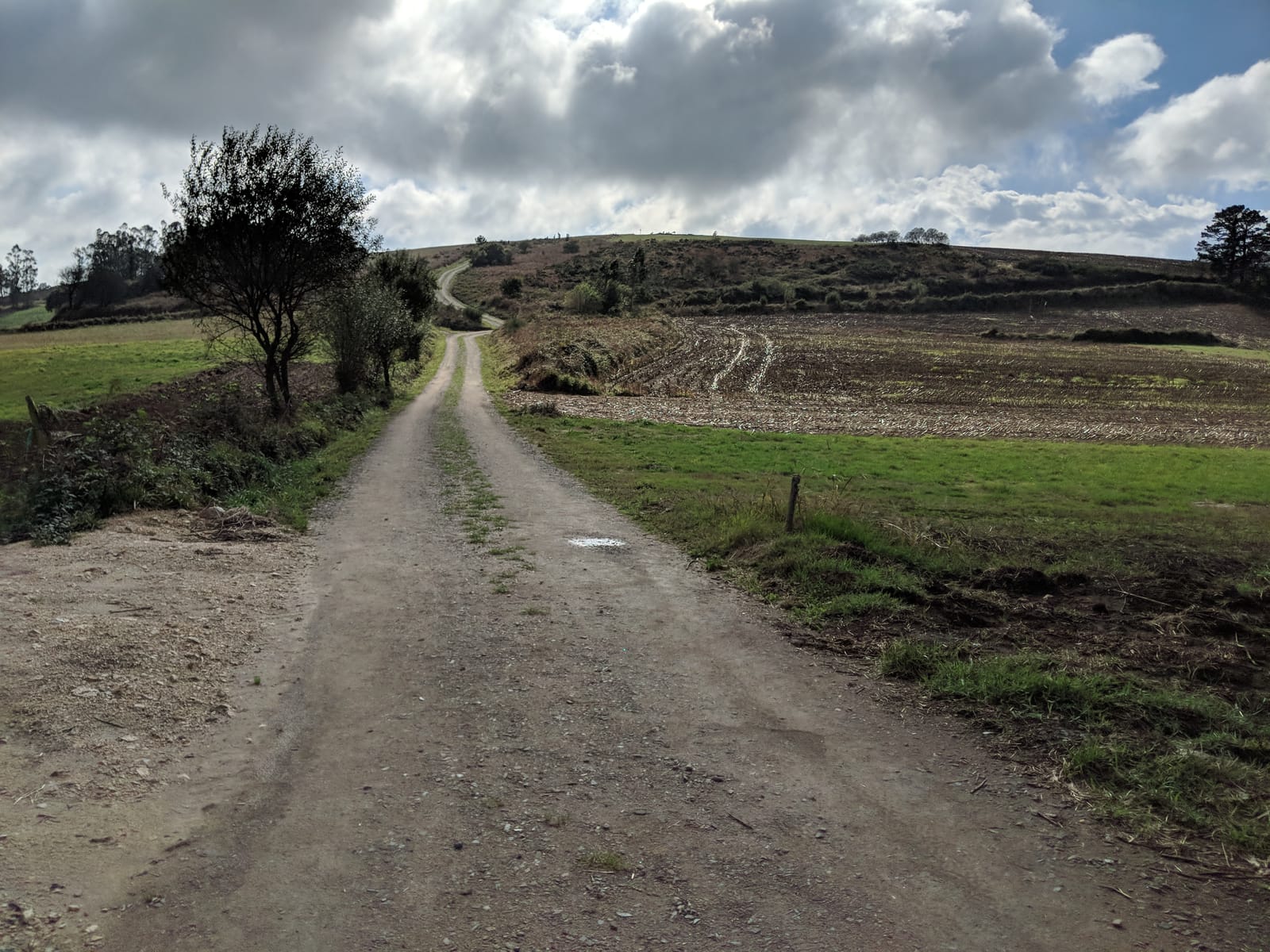 A gravel track climbing a bare hill under dramatic clouds