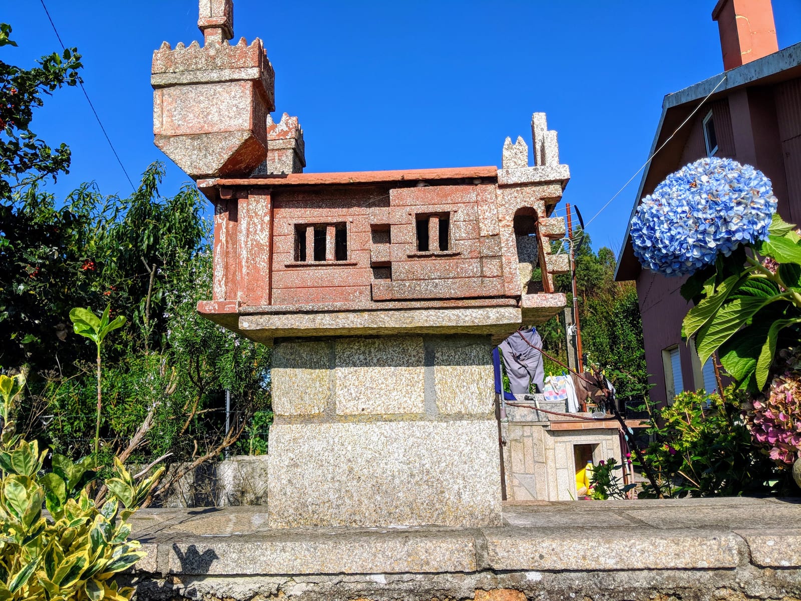 Granite hórreo beside a blue hydrangea in a garden