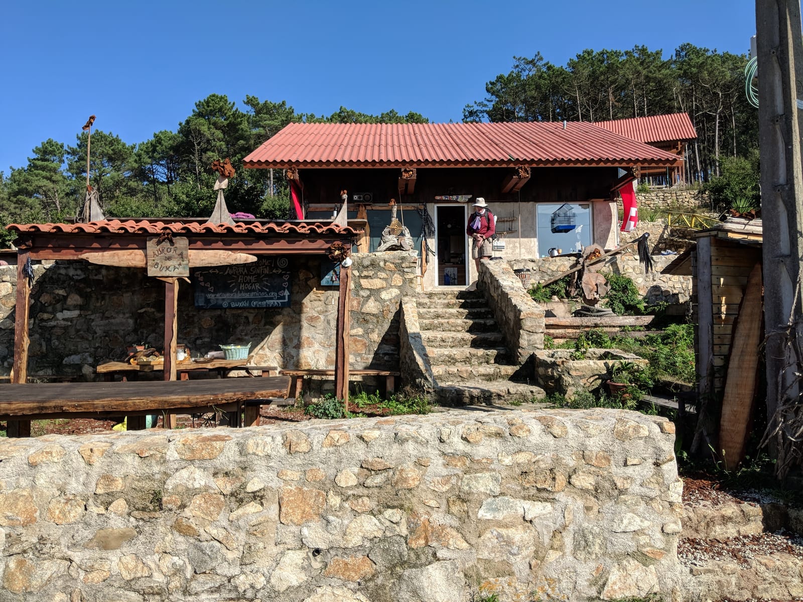 A quirky driftwood-decorated stone rest stop above the trail with hand-painted signs reading Home Hogar