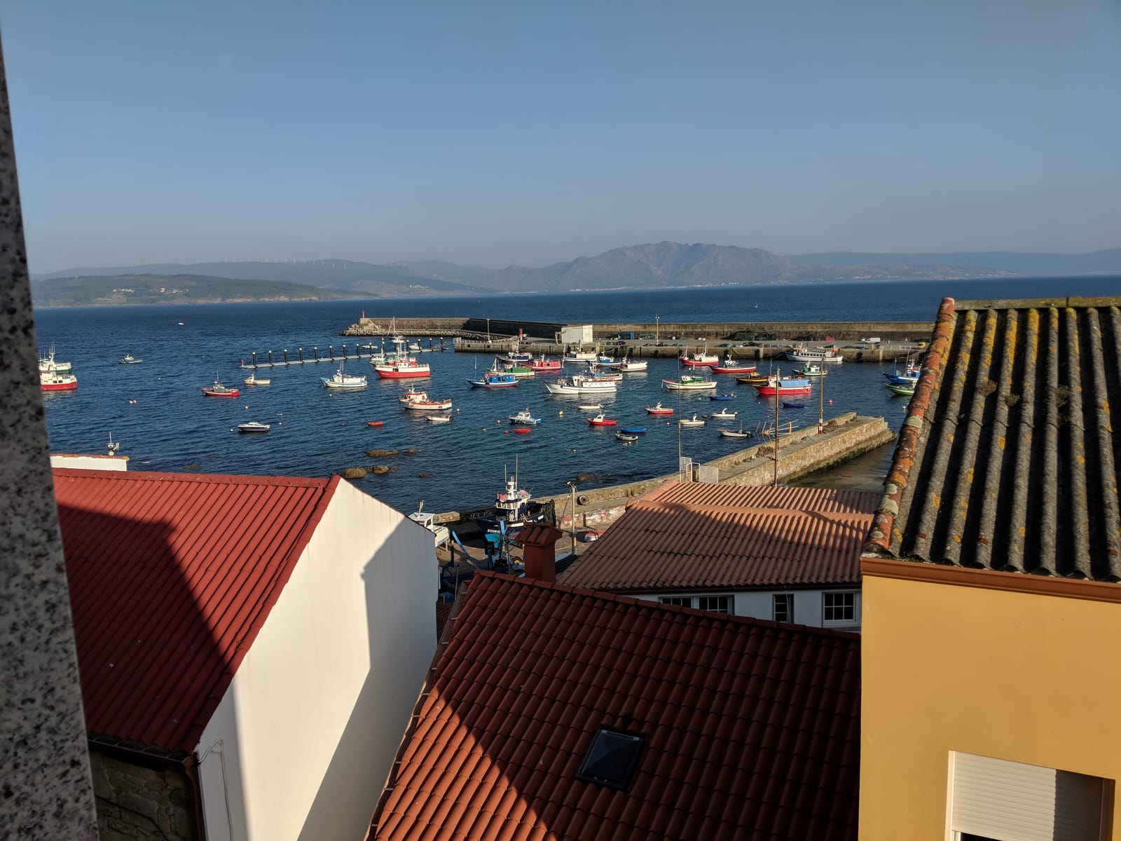 Finisterre's harbor full of colorful fishing boats, the cape and mountains across the bay