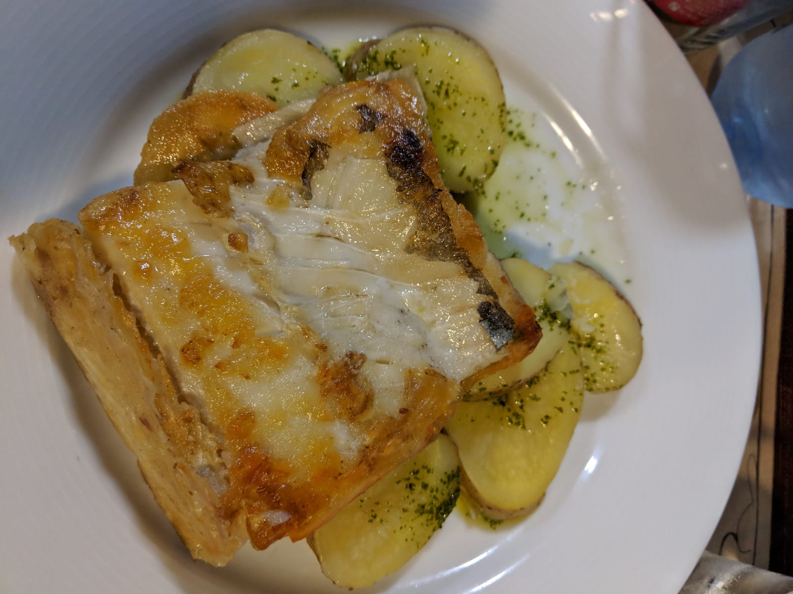 A plate of grilled white fish over sliced potatoes with parsley oil