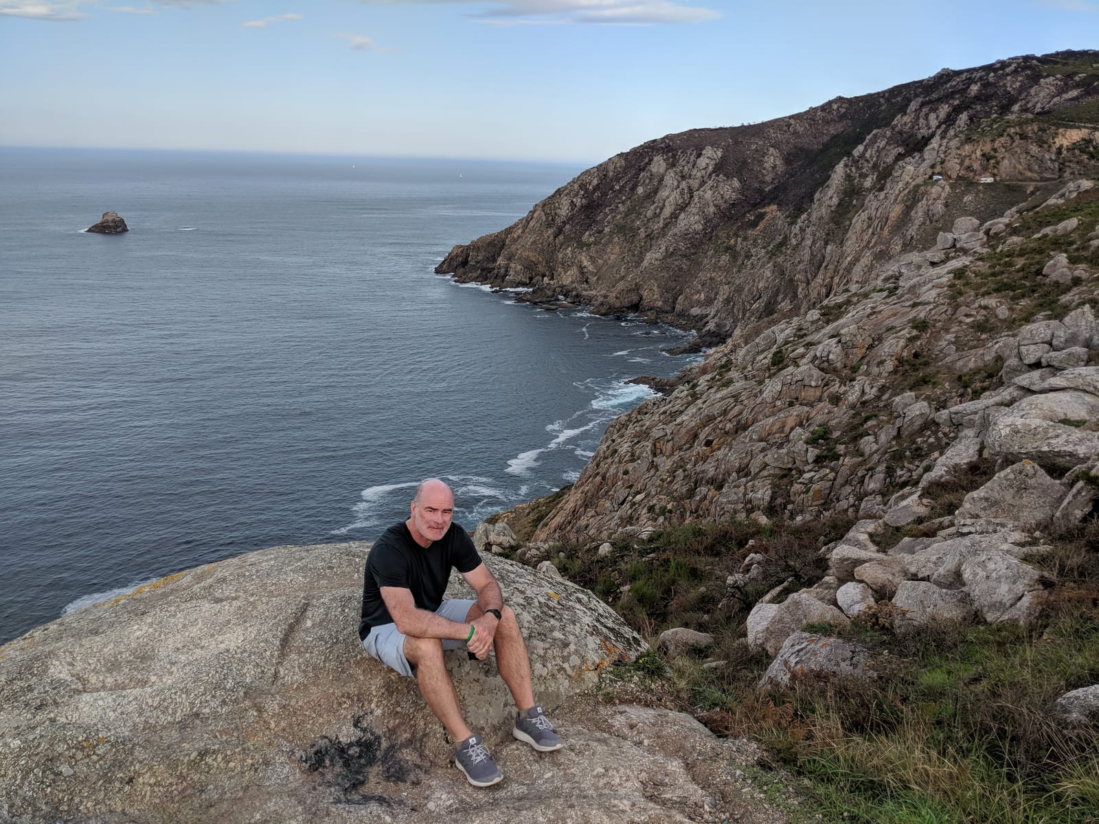 Doug sitting on a rock at the cliff's edge above the rugged Finisterre coast