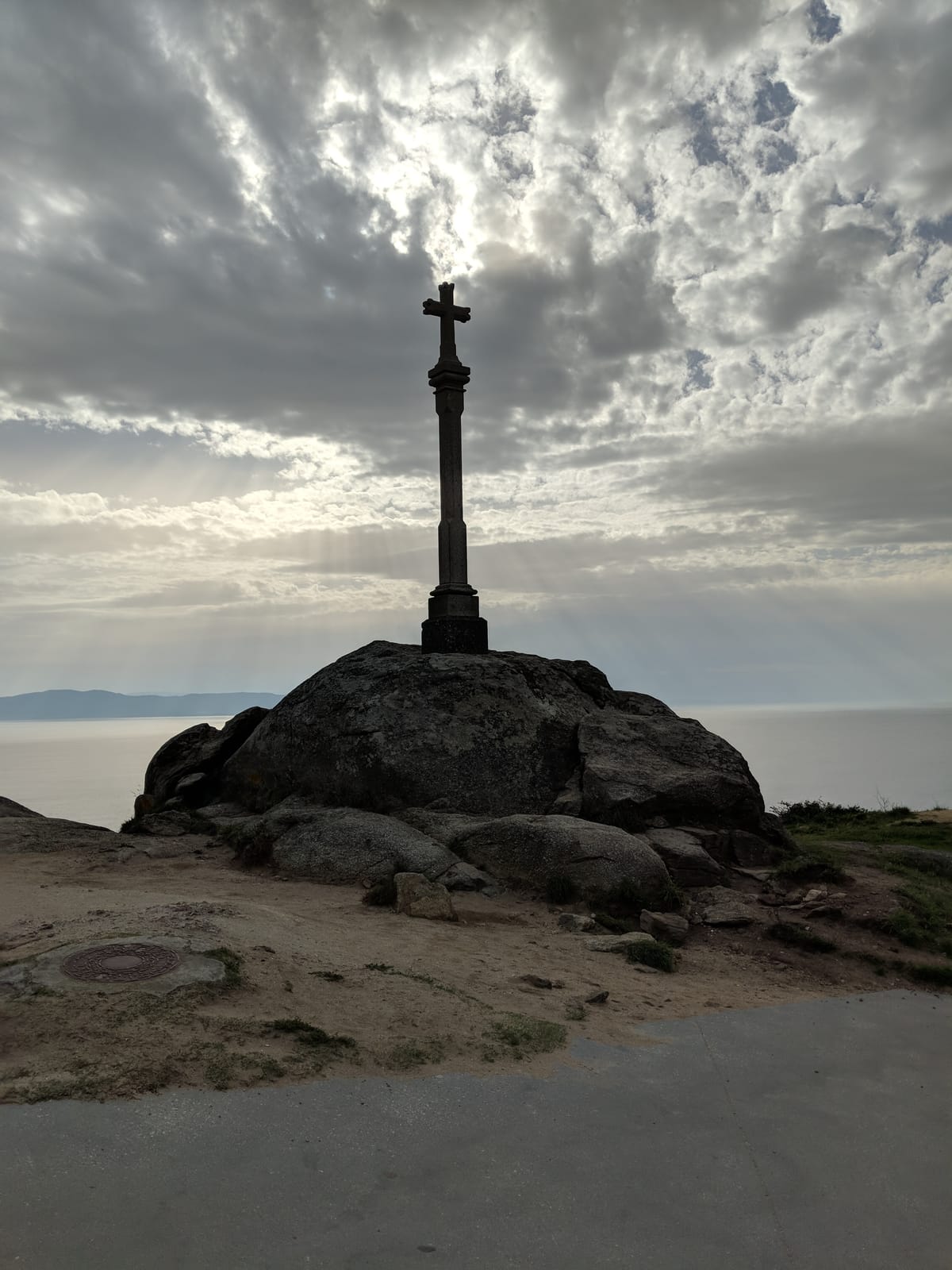Stone cruceiro cross on a boulder at Cape Finisterre, silhouetted against a dramatic sky