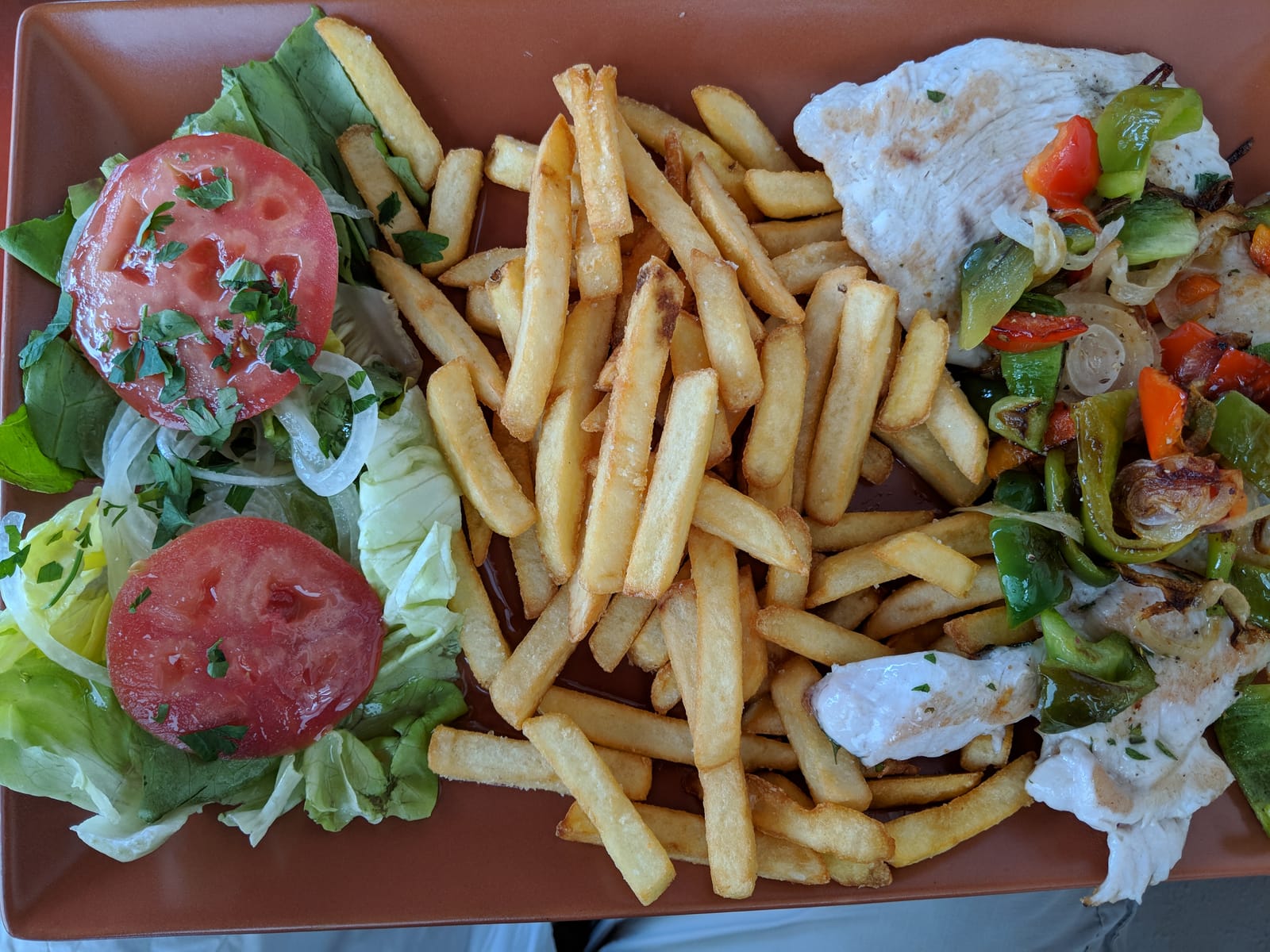 A harborside lunch plate of grilled chicken with peppers, fries, and a tomato salad