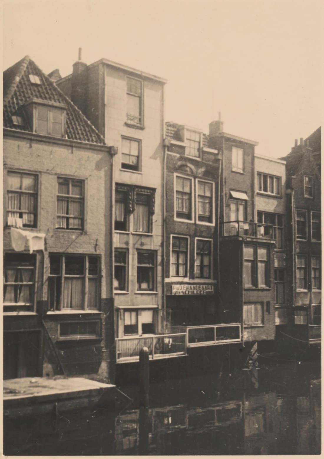 Sepia photograph of the backs of Voorstraat houses rising straight from the water of the Wijnhaven; at the far left a house with a tiled roof and a dormer window, beside a stone landing at the water's edge