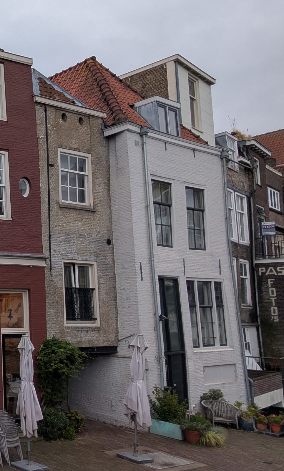 Close view of the back of Voorstraat 267 from the quay: a white-painted brick house with tall windows and a door at quay level, beside an older grey-brown brick house with two small round openings near its roofline