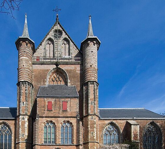 The west front of the Pieterskerk in Leiden, red brick with two slender corner towers and a red door, under a blue sky