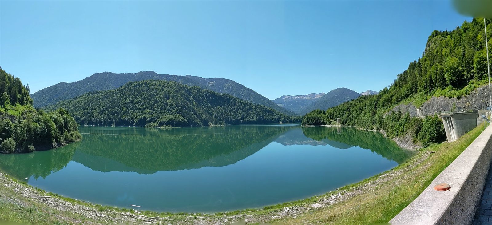 Panorama of the turquoise Sylvenstein reservoir with mountains mirrored in still water and the dam at right