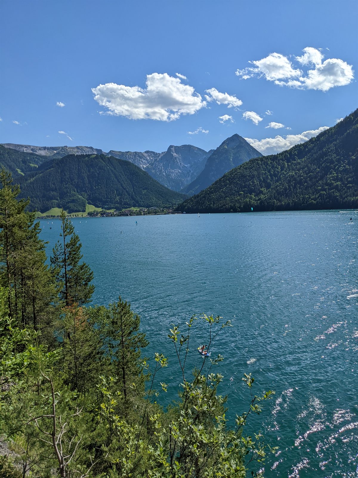 Elevated view from the lakeside path down onto the turquoise Achensee and a lone paddleboarder