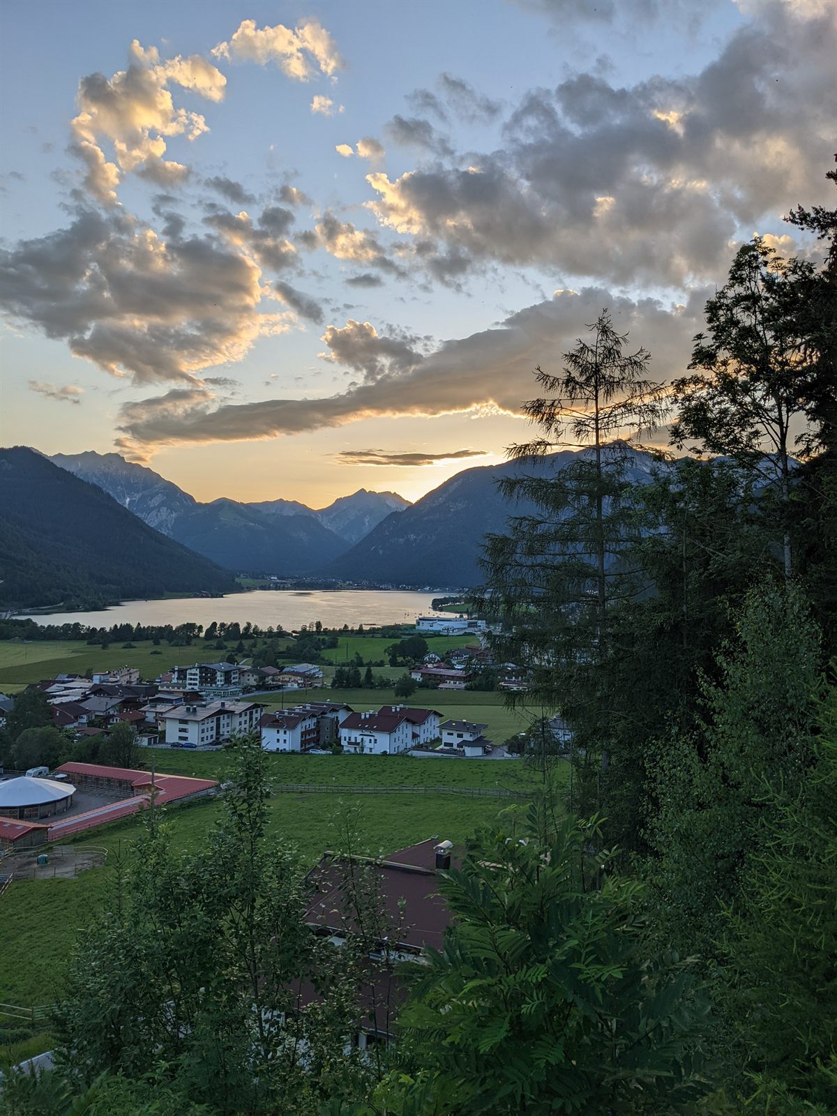 Sunset over the Achensee seen from above, the town below and the sun dropping behind the mountains