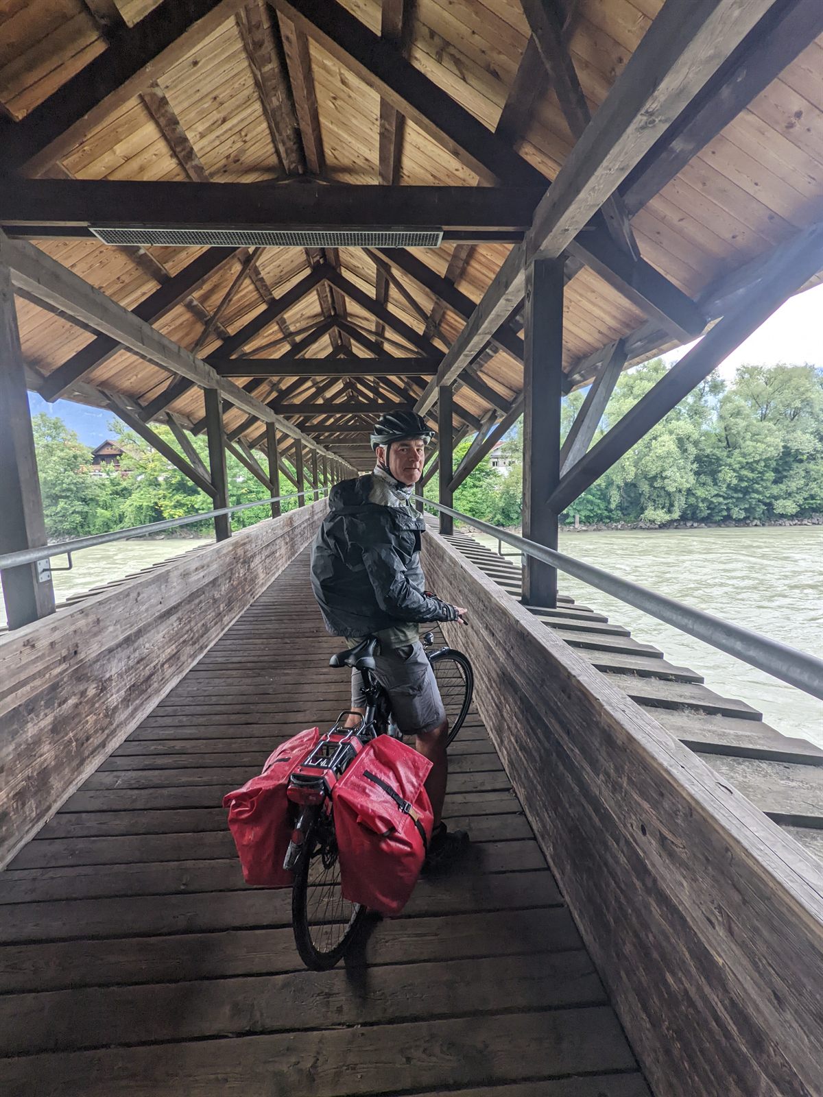 Doug on his loaded bike inside a covered wooden footbridge over the milky-green Inn river