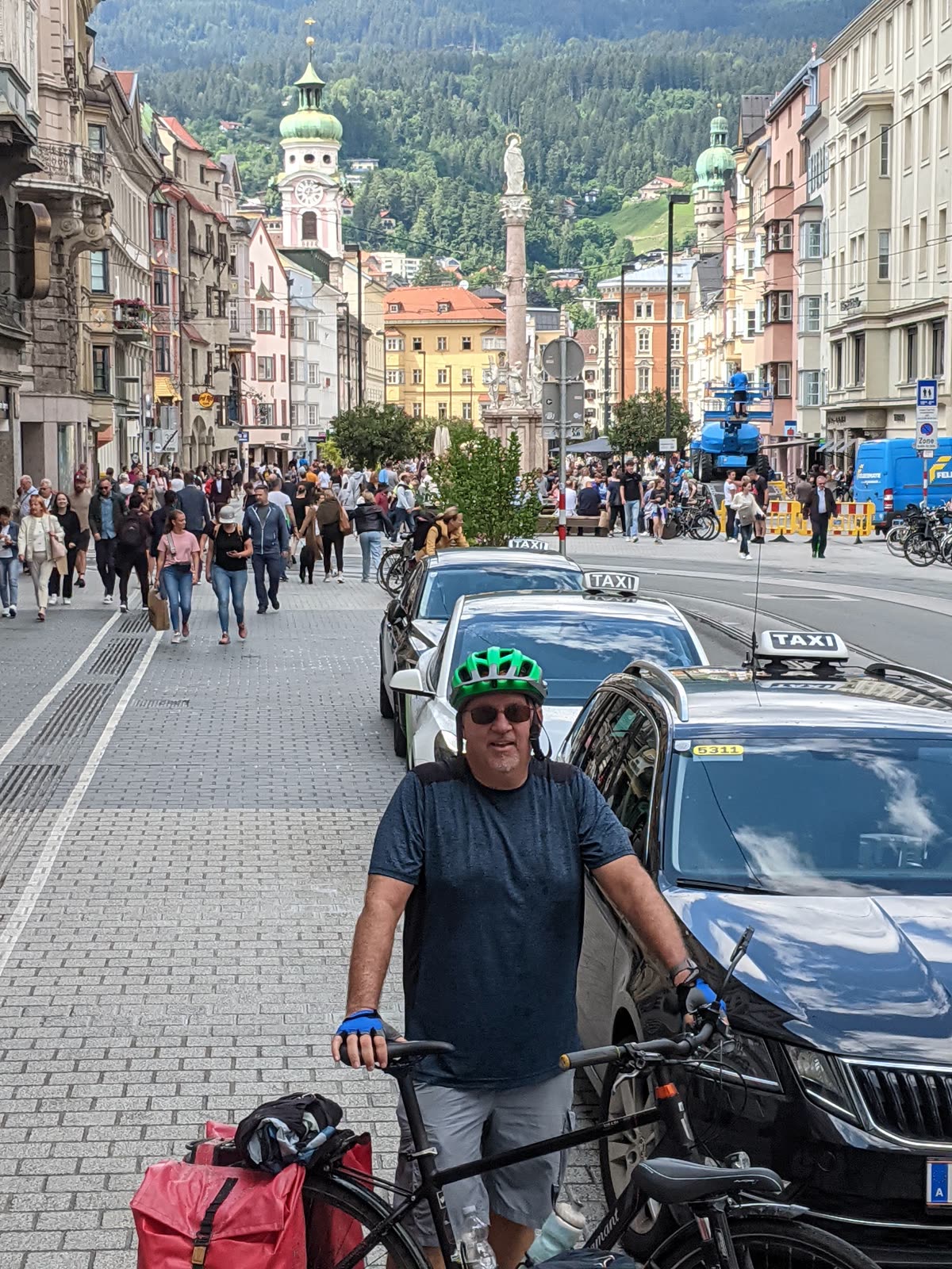 Mike walking his loaded touring bike along Innsbruck's Maria-Theresien-Straße, the Annasäule column and the Nordkette mountains behind