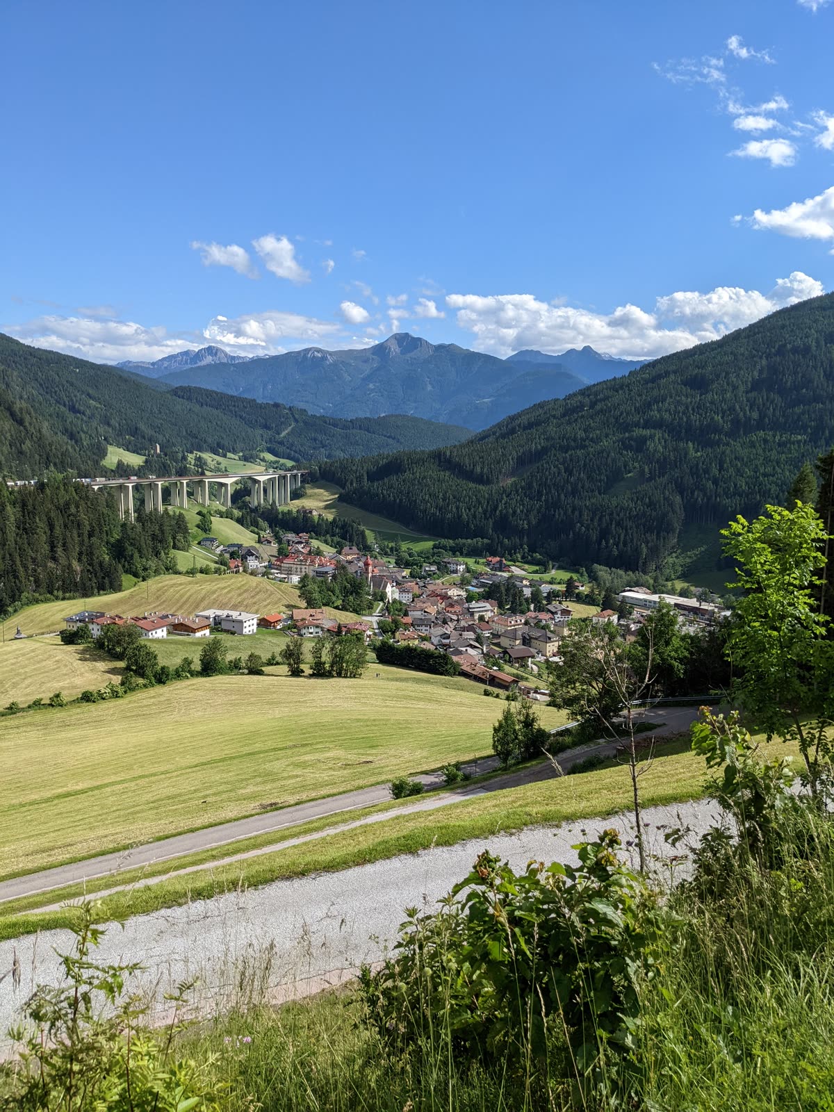 South Tyrol village of Colle Isarco in a green valley below, the Brenner autobahn viaduct crossing the slope above it