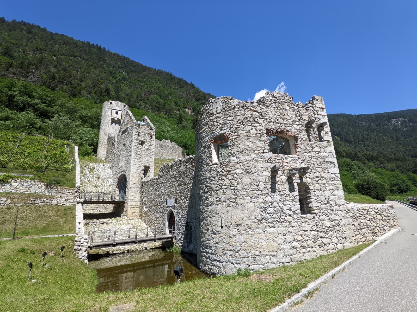 Round stone bastion of the Mühlbacher Klause beside a water-filled moat and footbridge, the road running past on the right