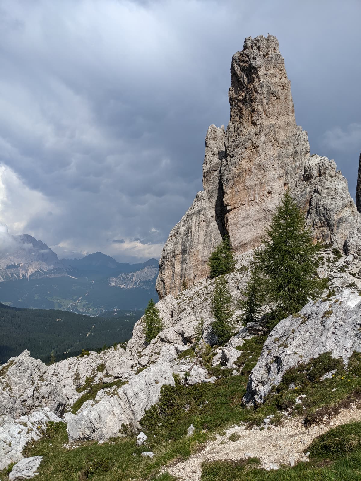 Towering pale Dolomite rock spire of the Cinque Torri under a heavy grey storm sky, dark rain sweeping across the distant valley below