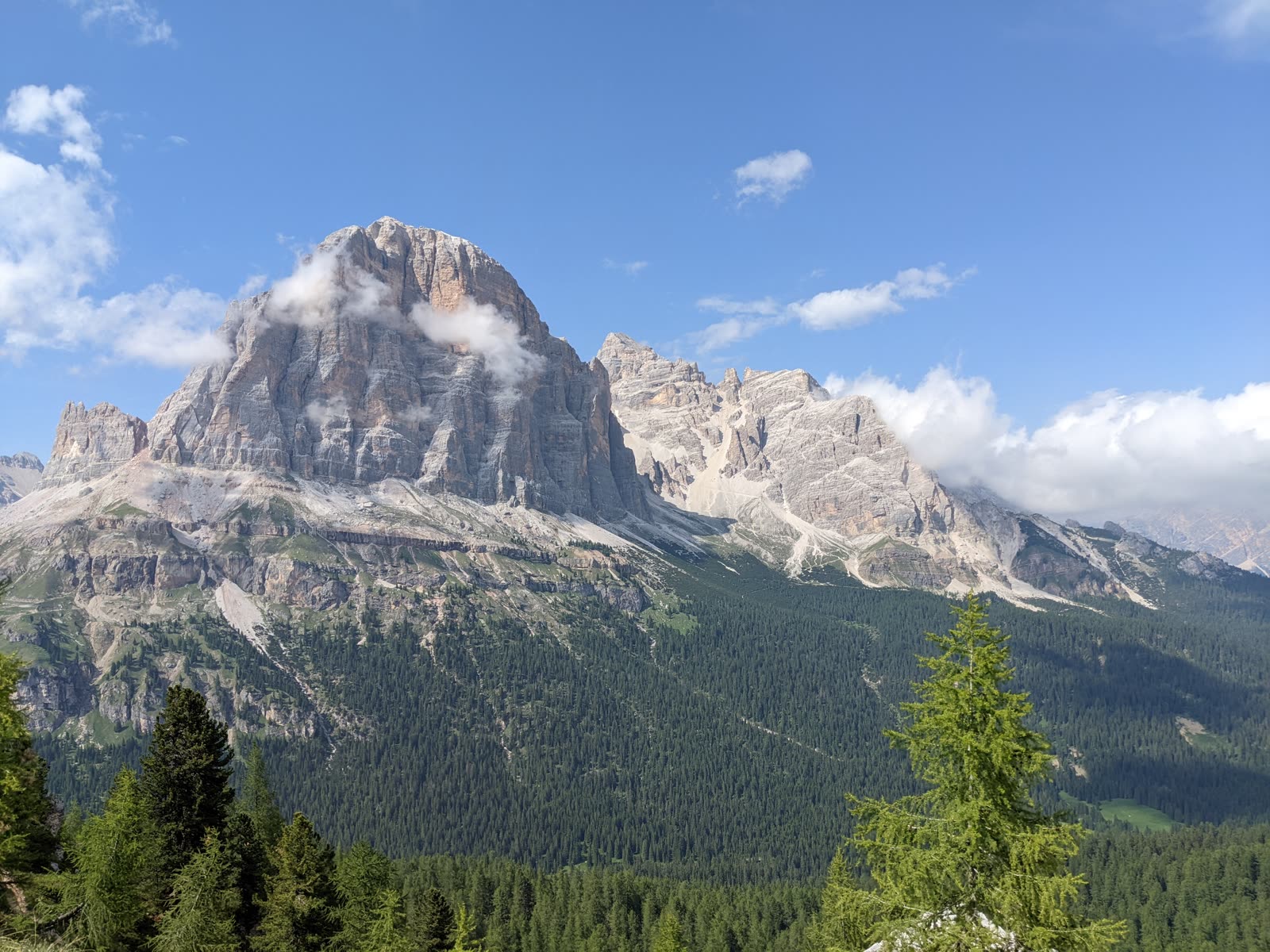 The great rounded bulk of the Tofana massif rising above dark forested slopes, wisps of cloud snagging on its pale rock face