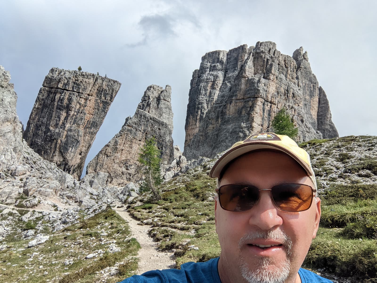 Mike in a tan cap and sunglasses taking a selfie in front of the pale Cinque Torri rock towers