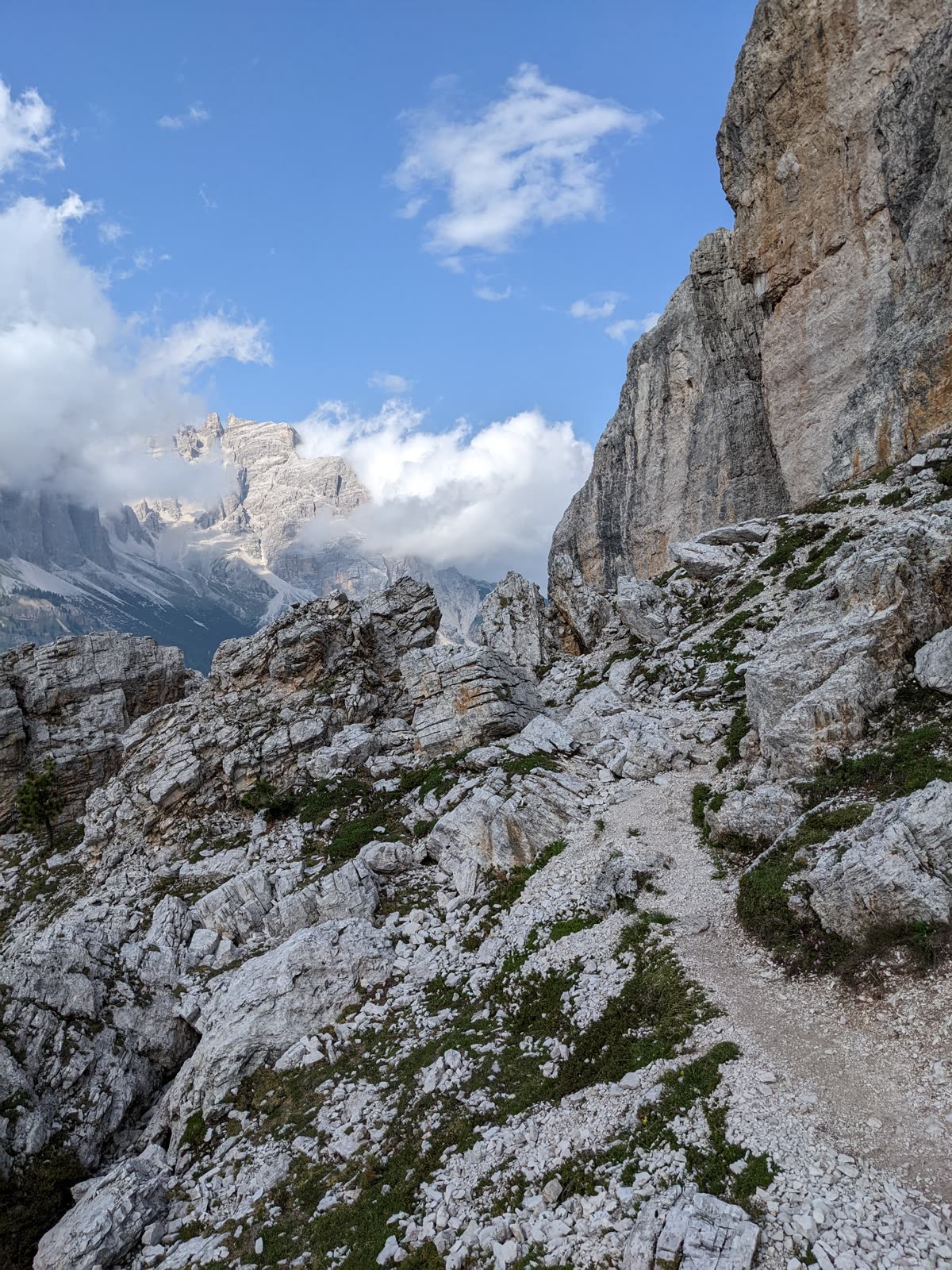 Rocky footpath threading through pale broken limestone of the Cinque Torri, cloud boiling up off the rock walls under blue sky
